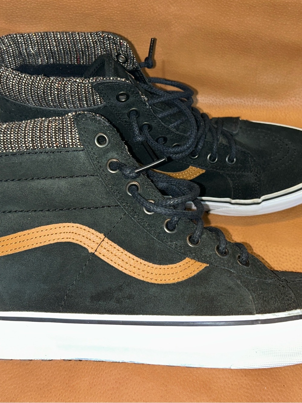 Black suede Vans Sk8-Hi high-top sneakers with a tweed-patterned collar.